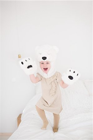 simsearch:6102-07842733,k - Girl wearing polar bear costume jumping on bed Foto de stock - Royalty Free Premium, Número: 6102-07842733