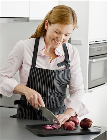 simsearch:6102-08885673,k - Smiling woman cutting onion in kitchen Stock Photo - Premium Royalty-Free, Code: 6102-07842888