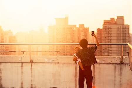 simsearch:6102-08388194,k - Woman with baby on roof, cityscape at sunset on background Foto de stock - Royalty Free Premium, Número: 6102-08001498