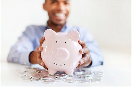 simsearch:6102-08168957,k - Young man putting coin in piggybank Stock Photo - Premium Royalty-Free, Code: 6102-08168954