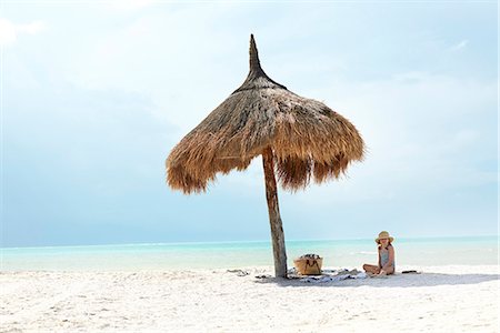 simsearch:6102-08996069,k - Girl sitting on beach under thatched umbrella Stock Photo - Premium Royalty-Free, Code: 6102-08388310