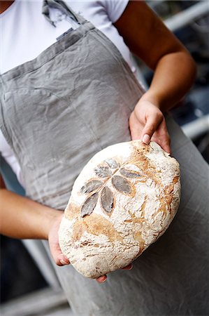 Female baker holding fresh bread with leaf pattern Stock Photo - Premium Royalty-Free, Code: 6102-08388318