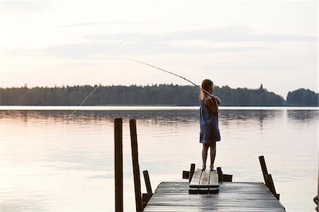 Girl standing on jetty with fishing net - Stock Photo - Masterfile