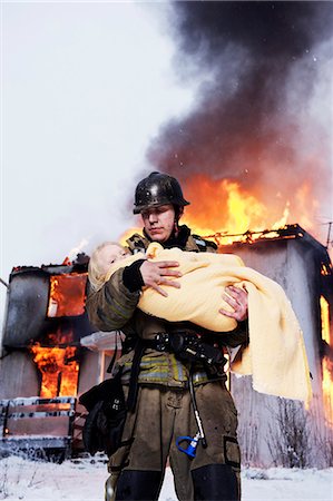 Fireman holding rescued girl, burning building in background Foto de stock - Royalty Free Premium, Número: 6102-08558959