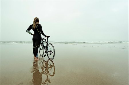 en pied - Young woman wearing wetsuit and standing with bike on beach Photographie de stock - Premium Libres de Droits, Code: 6102-08558967