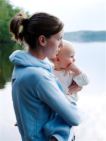 simsearch:6102-08885644,k - A woman standing by a lake and holding a baby, Sweden. Foto de stock - Royalty Free Premium, Número: 6102-08559522