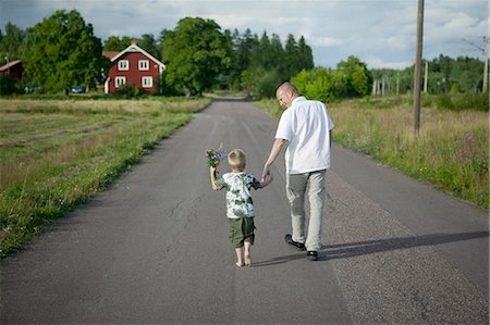 simsearch:6102-08761067,k - Father walking with son on road, boy holding flowers Fotografie stock - Premium Royalty-Free, Codice: 6102-08746491