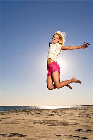 simsearch:6102-06336949,k - Happy young woman jumping on beach Fotografie stock - Premium Royalty-Free, Codice: 6102-08746506