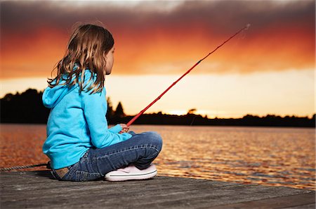 Premium Photo  Little girl in straw hat sitting on the edge of a wooden  dock and fishing in lake at sunset.