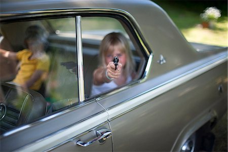 A girl with a toy gun in the rearseat of a car Stock Photo - Premium Royalty-Free, Code: 6102-08761290