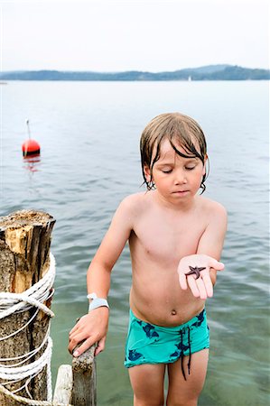 Boy on jetty holding starfish Stock Photo - Premium Royalty-Free, Code: 6102-08761465