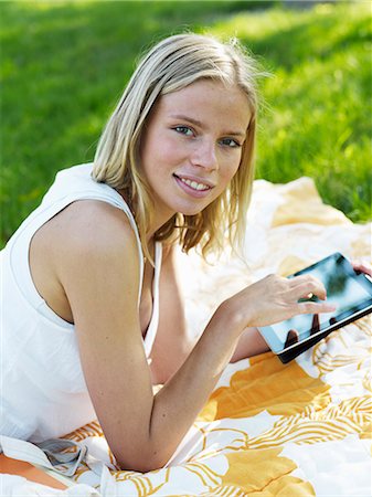simsearch:6102-08746546,k - Young woman lying on blanket holding digital tablet, smiling, portrait Photographie de stock - Premium Libres de Droits, Code: 6102-08800332