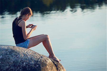 Teenage girl sitting and using cell phone by lake Stock Photo - Premium Royalty-Free, Code: 6102-08952071