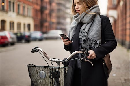 simsearch:6102-07768969,k - Young woman with bicycle looking at cell phone Foto de stock - Royalty Free Premium, Número: 6102-08996377