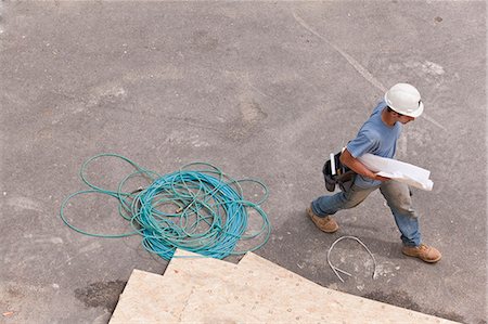 Carpenter walking at a construction site with building plans Stock Photo - Premium Royalty-Free, Code: 6105-05395982