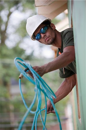 Carpenter passing coiled air hose through the window of a house under construction Stock Photo - Premium Royalty-Free, Code: 6105-05396158