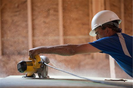Hispanic carpenter using a circular saw on the roofing sheathing at a house under construction Stock Photo - Premium Royalty-Free, Code: 6105-05396168