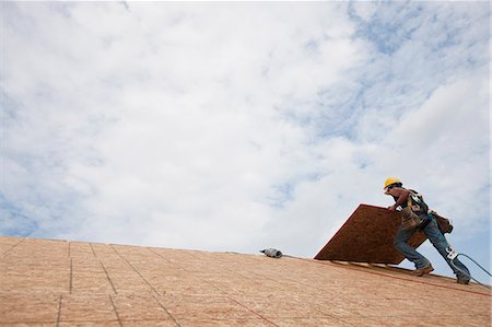 simsearch:6105-05396235,k - Low angle view of a carpenter lifting a roof panel on the roof of a house under construction Foto de stock - Royalty Free Premium, Número: 6105-05396133