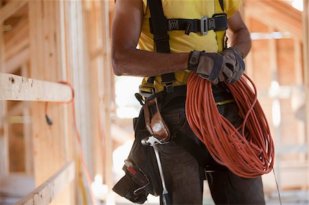 simsearch:6105-05396204,k - Hispanic carpenter coiling electrical power cord at a construction site Stock Photo - Premium Royalty-Free, Code: 6105-05396252