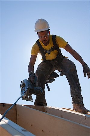 simsearch:6105-05396266,k - Hispanic carpenter using a circular saw on the roof beams at a house under construction Foto de stock - Royalty Free Premium, Número: 6105-05396261