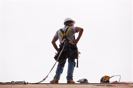 Hispanic carpenter standing on the roofing with a hammer, circular saw and a nail gun Fotografie stock - Premium Royalty-Free, Codice: 6105-05396289