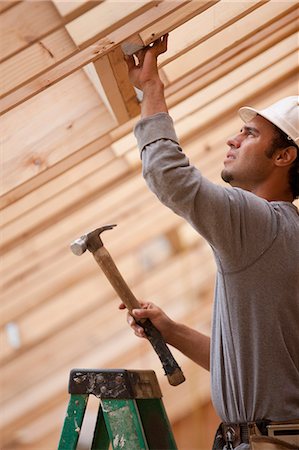 simsearch:6105-05396204,k - Hispanic carpenter hammering metal reinforcement bracing at a house under construction Stock Photo - Premium Royalty-Free, Code: 6105-05396205