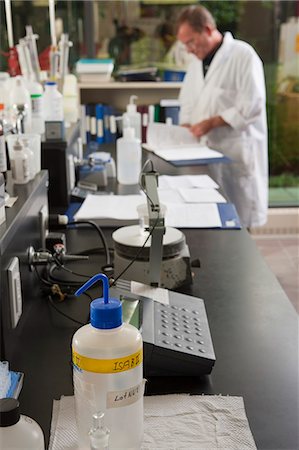 simsearch:6105-05396454,k - Flasks and reagent bottles on a laboratory bench with a scientist in the background Stock Photo - Premium Royalty-Free, Code: 6105-05396467