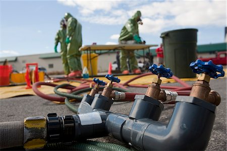 Tubulure de distribution de l'eau dans la zone de décontamination de matières dangereuses avec les pompiers de matières dangereuses en arrière-plan Photographie de stock - Premium Libres de Droits, Code: 6105-05396524