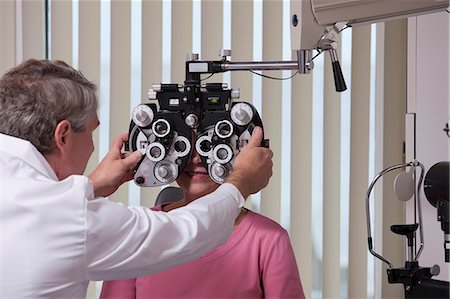 eye test - Ophthalmologist placing phoropter in front of a female patient Foto de stock - Sin royalties Premium, Código: 6105-05396646