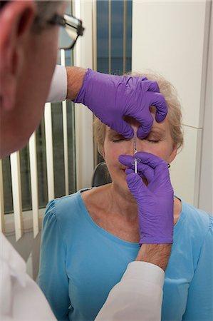 Ophthalmologist giving a Botox injection in glabellar region of the forehead of a patient Stock Photo - Premium Royalty-Free, Code: 6105-05396656