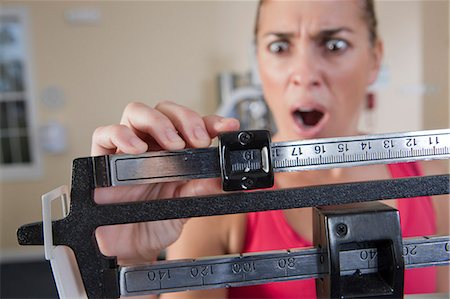 Woman weighing herself on a weighing scale and looking shocked Foto de stock - Sin royalties Premium, Código: 6105-05396673