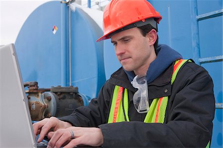 Engineer recording data on a laptop near a fuel tankers site Stock Photo - Premium Royalty-Free, Code: 6105-05396979