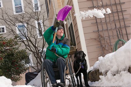 Femme avec une sclérose en plaques, pelleter de la neige dans un fauteuil roulant avec un chien d'assistance Photographie de stock - Premium Libres de Droits, Code: 6105-05397015