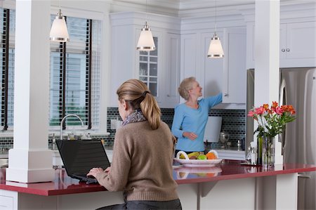 sitting looking at backside - Women in kitchen of a Green Technology Home with energy efficiency appliances, stone countertops, and recycled wood Stock Photo - Premium Royalty-Free, Code: 6105-05397279