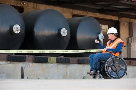Facilities engineer in a wheelchair pulling caution tape in front of chemical storage tanks Foto de stock - Royalty Free Premium, Número: 6105-05953715
