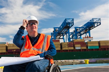 Transportation engineer in a wheelchair studying plans at shipping port Stock Photo - Premium Royalty-Free, Code: 6105-05953722