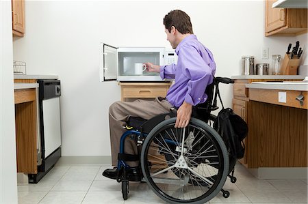 simsearch:6105-07744517,k - Man in wheelchair with spinal cord injury removing cup from an accessible microwave Fotografie stock - Premium Royalty-Free, Codice: 6105-06042960