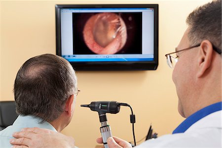 Audiologist doing live video inspection of ear canal while a patient watches on a computer screen Foto de stock - Sin royalties Premium, Código: 6105-06042967