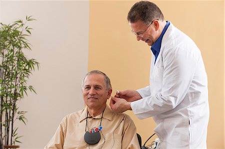 expert (male) - Audiologist inserting behind-the-ear hearing aid into a patient's ear during programming Stock Photo - Premium Royalty-Free, Code: 6105-06042975