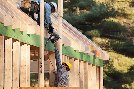 power tool - Carpenter handing nail gun to another carpenter on roof Stock Photo - Premium Royalty-Free, Code: 6105-06042985