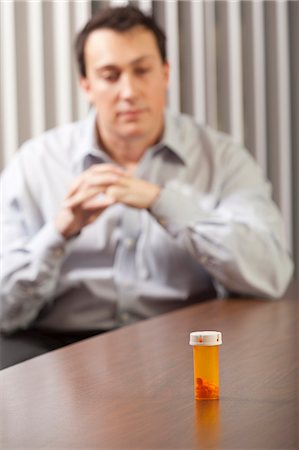 Businessman at desk looking at a pill bottle Stock Photo - Premium Royalty-Free, Code: 6105-06043072