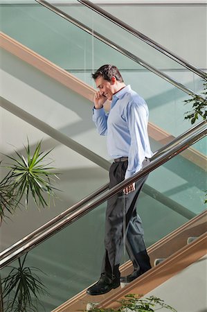 Businessman talking on mobile phone walking down stairs Stock Photo - Premium Royalty-Free, Code: 6105-06043083