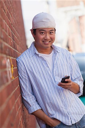 smiling chinese man with cap - Chinese student reading text messages on cell phone Stock Photo - Premium Royalty-Free, Code: 6105-06702866