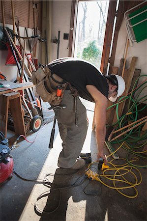 simsearch:6105-06702940,k - Hispanic carpenter plugging in rechargeable battery in home garage Stock Photo - Premium Royalty-Free, Code: 6105-06702891
