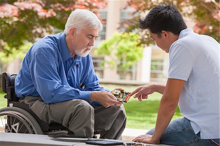 Engineer with muscular dystrophy and diabetes in his wheelchair talking with design engineer about microchips on circuit board Stock Photo - Premium Royalty-Free, Code: 6105-06702984