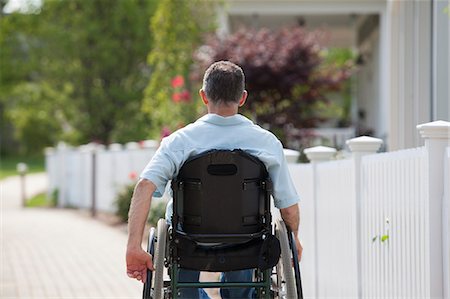simsearch:6105-05396581,k - Man with spinal cord injury in a wheelchair on a suburb walk with homes Photographie de stock - Premium Libres de Droits, Code: 6105-06703069