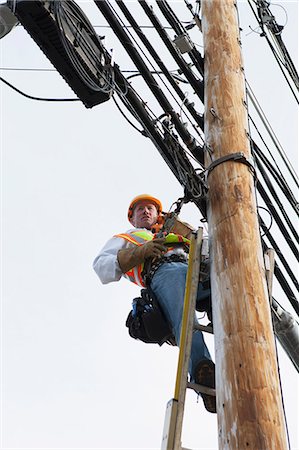 safety harness - Communications worker talking on butt set while installing new cables on power pole Stock Photo - Premium Royalty-Free, Code: 6105-07521262