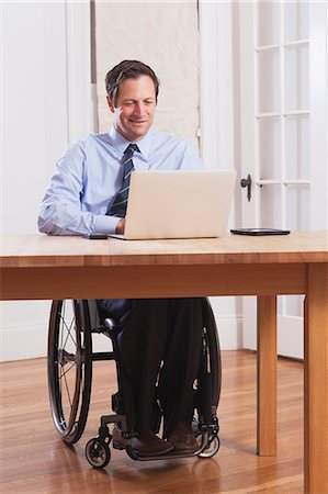 simsearch:6105-07744517,k - Businessman with spinal cord injury in a wheelchair working on laptop Fotografie stock - Premium Royalty-Free, Codice: 6105-07521212