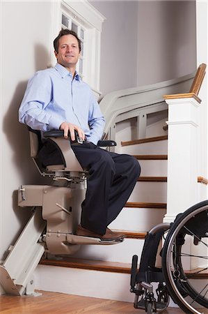 simsearch:6105-07744517,k - Man with spinal cord injury going up in his motorized stair lift Fotografie stock - Premium Royalty-Free, Codice: 6105-07521216