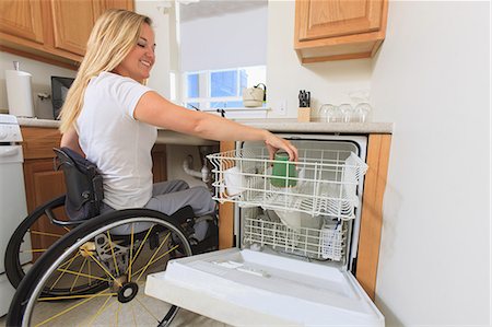 Woman with spinal cord injury in her accessible kitchen putting a cup in dishwasher Foto de stock - Royalty Free Premium, Número: 6105-07744366